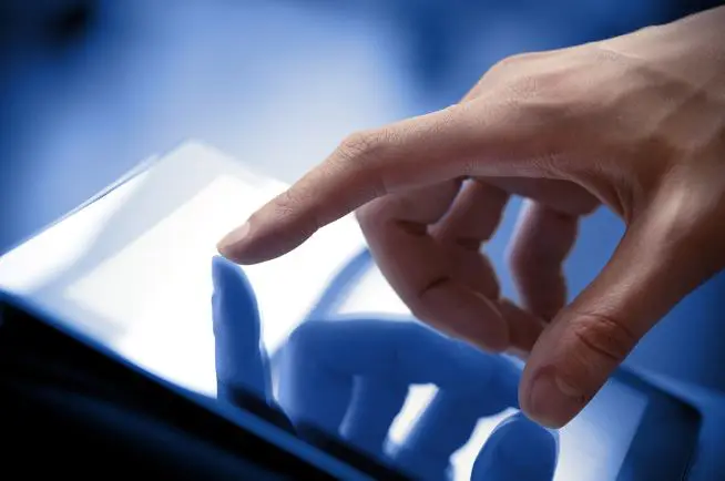 A hand touching a Projected Capacitive Touchscreen tablet with the index finger.