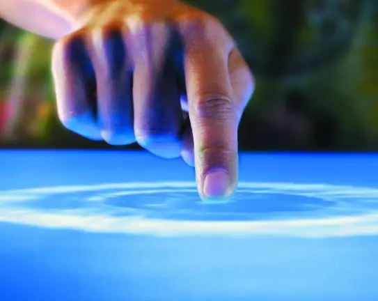 A finger touching a large resistive touch screen that is lighting up in response to the touch.